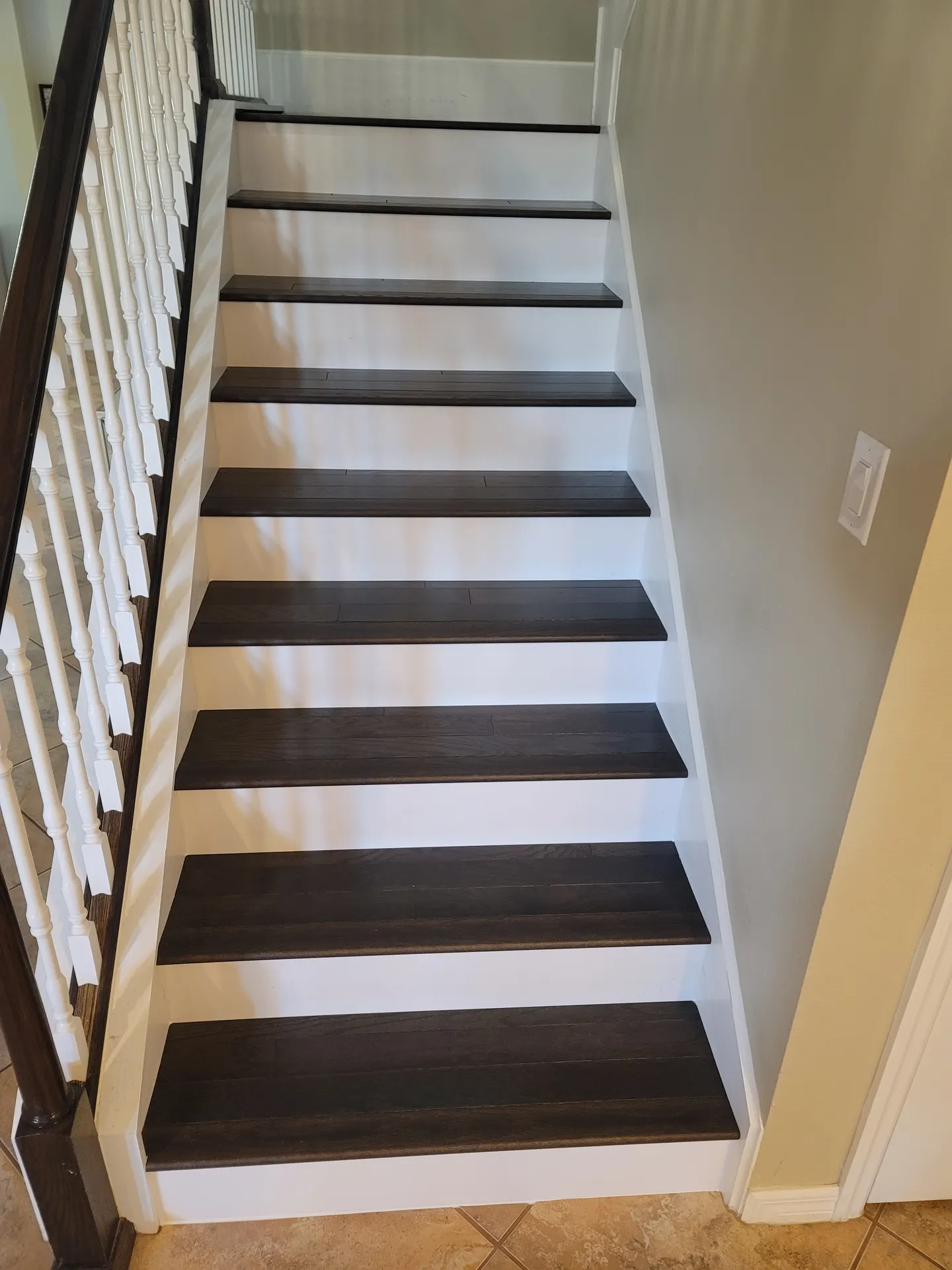 Staircase remodeled with dark-stained oak treads, crisp white risers and stringers, and white balusters under a dark wood handrail.