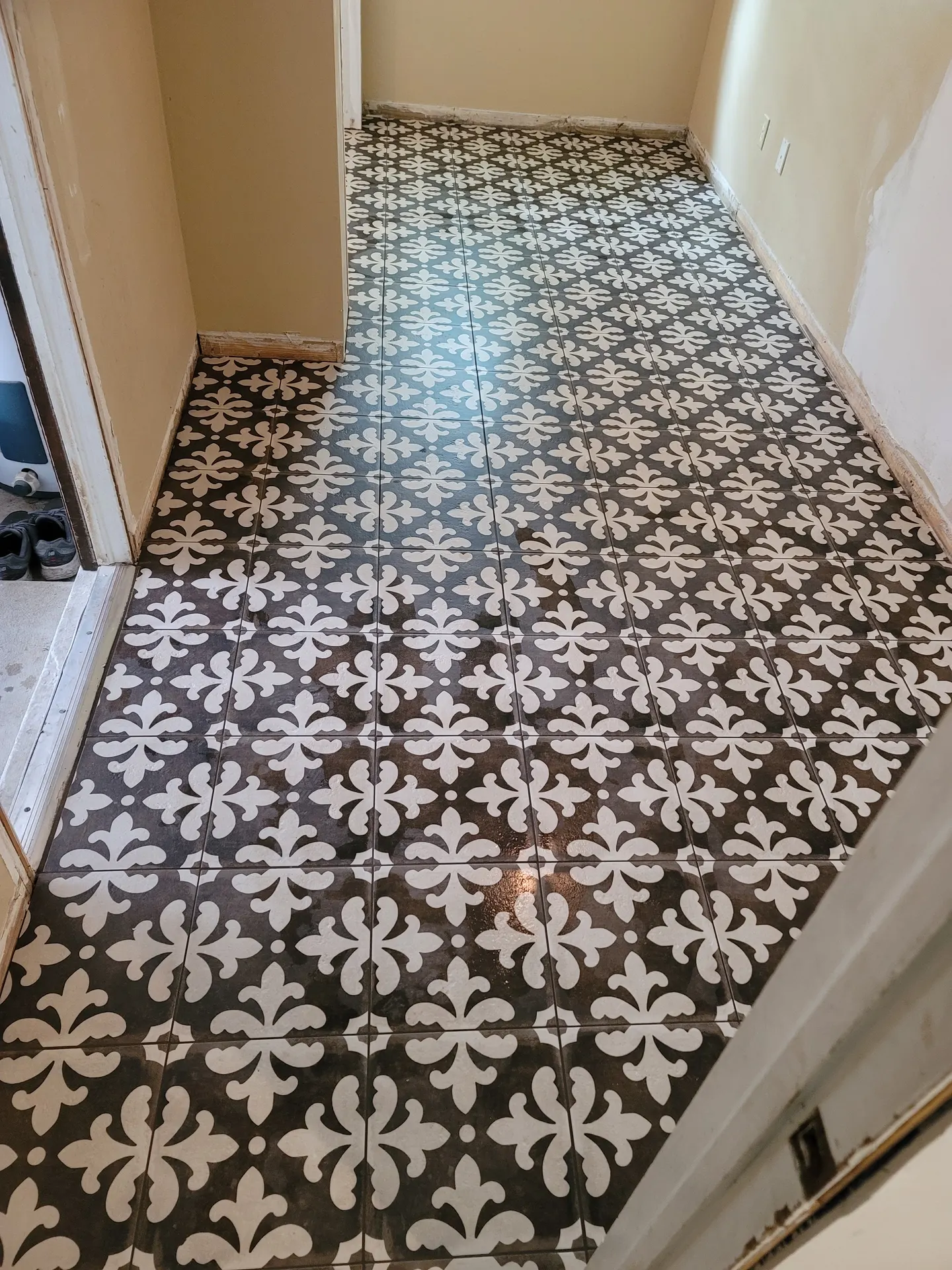 Vintage-style porcelain tile with a white fleur-de-lis pattern on a charcoal background installed in a bathroom under renovation.