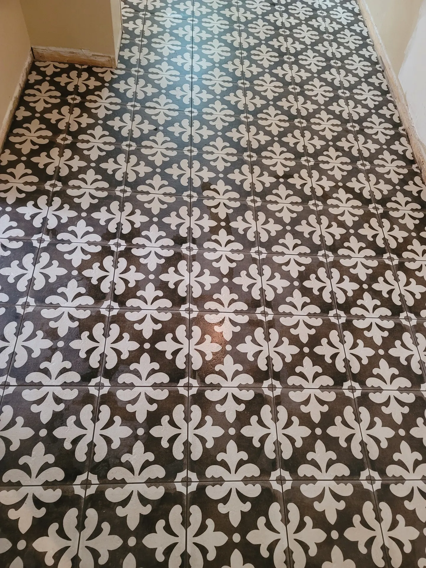 Close-up of straight-lay encaustic-look porcelain tile with a white fleur-de-lis motif on a dark charcoal background.