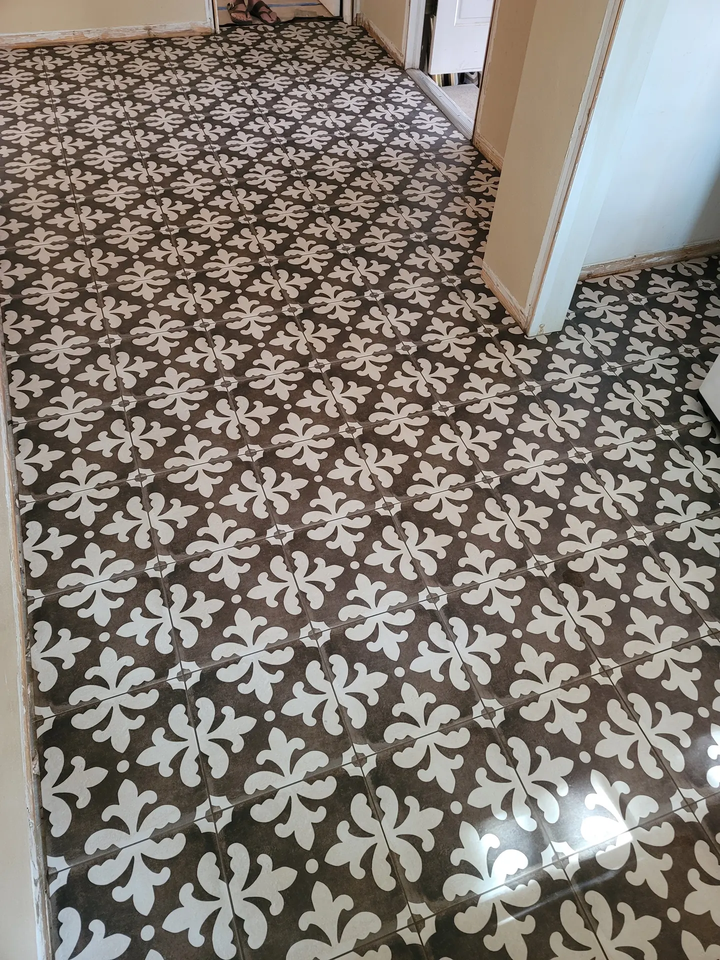 Patterned porcelain floor tile with a fleur-de-lis design in charcoal and white laid straight-set through a hallway during renovation.