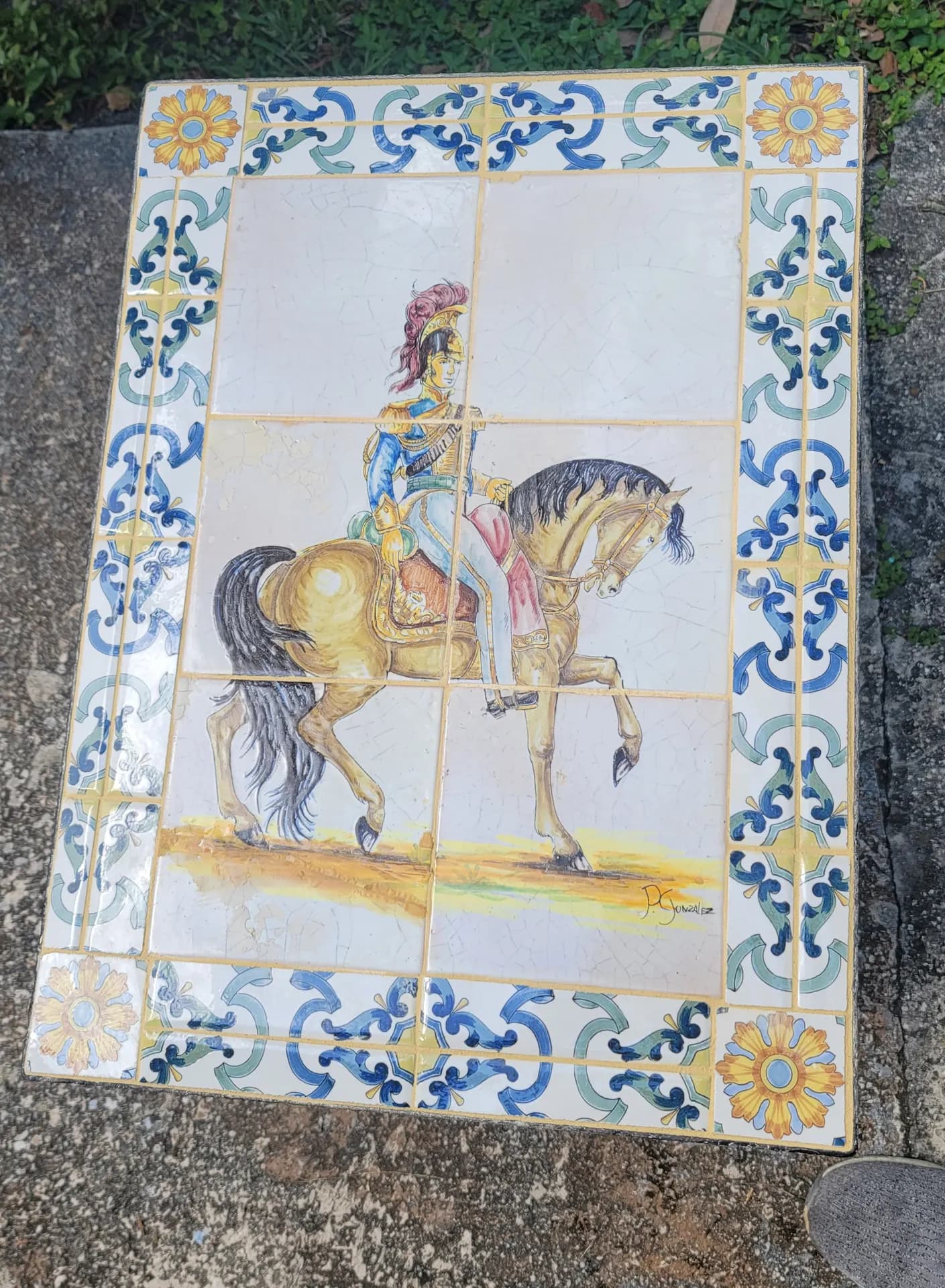 Hand-painted tile mural depicting a cavalry rider on horseback, bordered with traditional blue, green, and gold Spanish-style tiles.