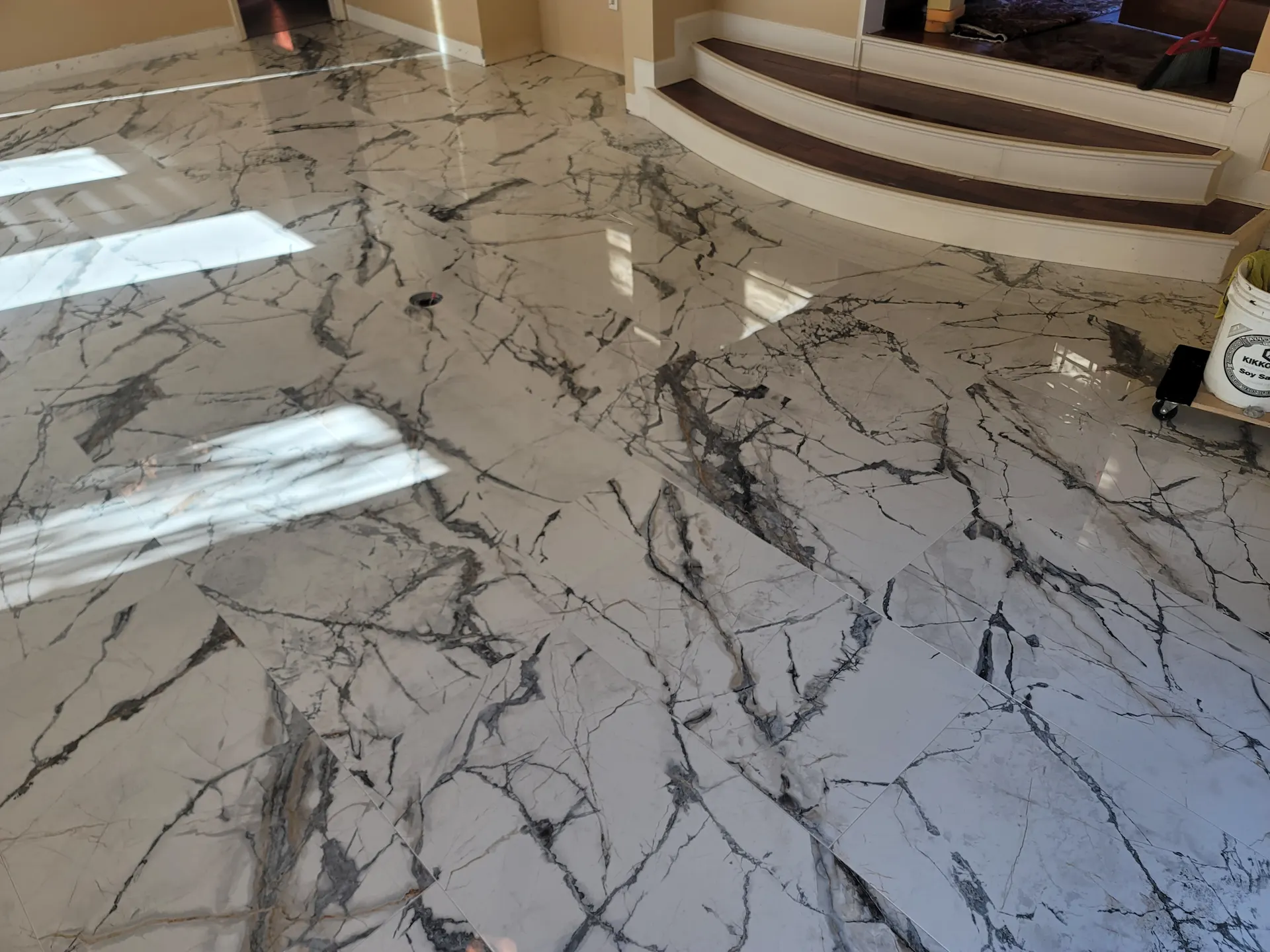 Open living area with polished large-format marble-look porcelain floor tile featuring dramatic gray veining, flowing toward curved wood steps.