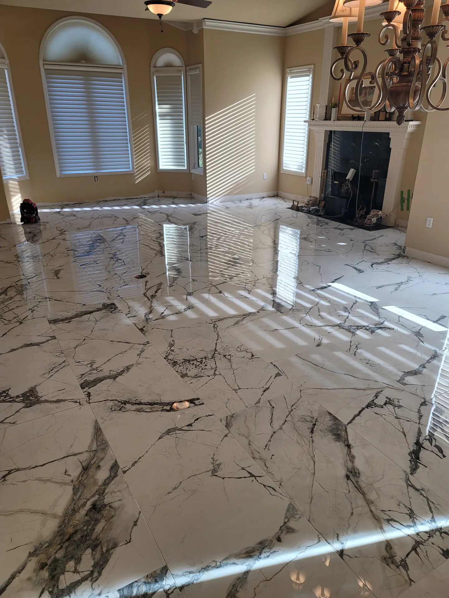 Sun-drenched great room with arched windows and a chandelier showcasing a polished marble-look porcelain tile floor in a straight-lay pattern.