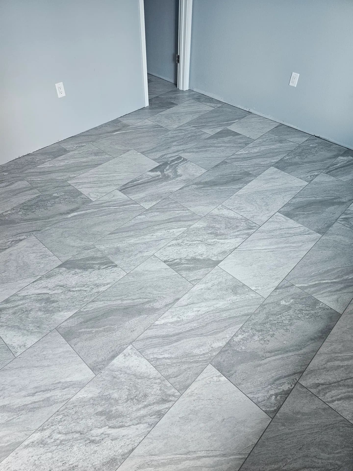 Gray marble-look porcelain tile floor laid in a modular mixed-size pattern in a freshly painted room with white trim.