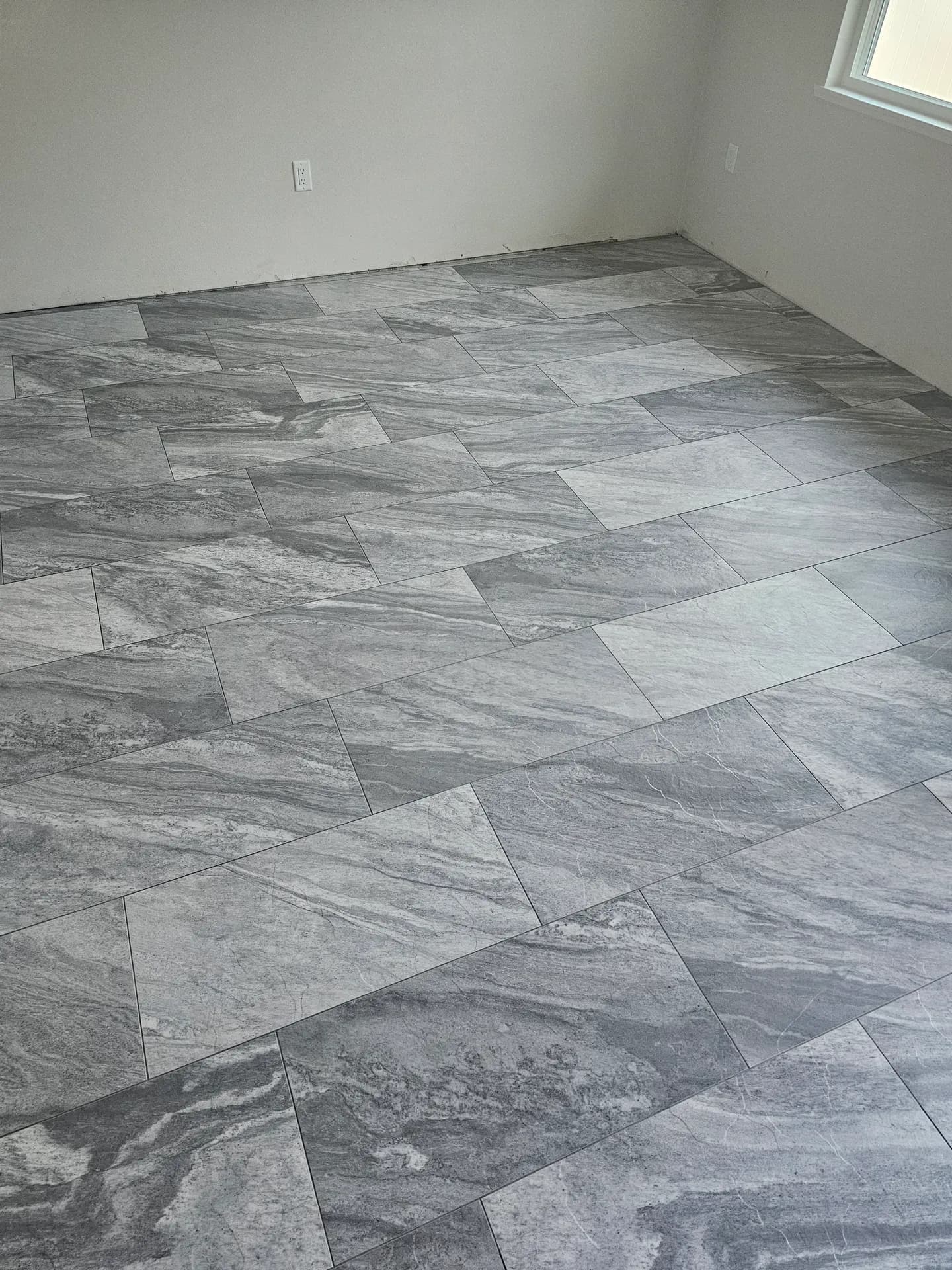 Wide view of a gray stone-look porcelain floor in an offset pattern filling a bright room with light gray walls.