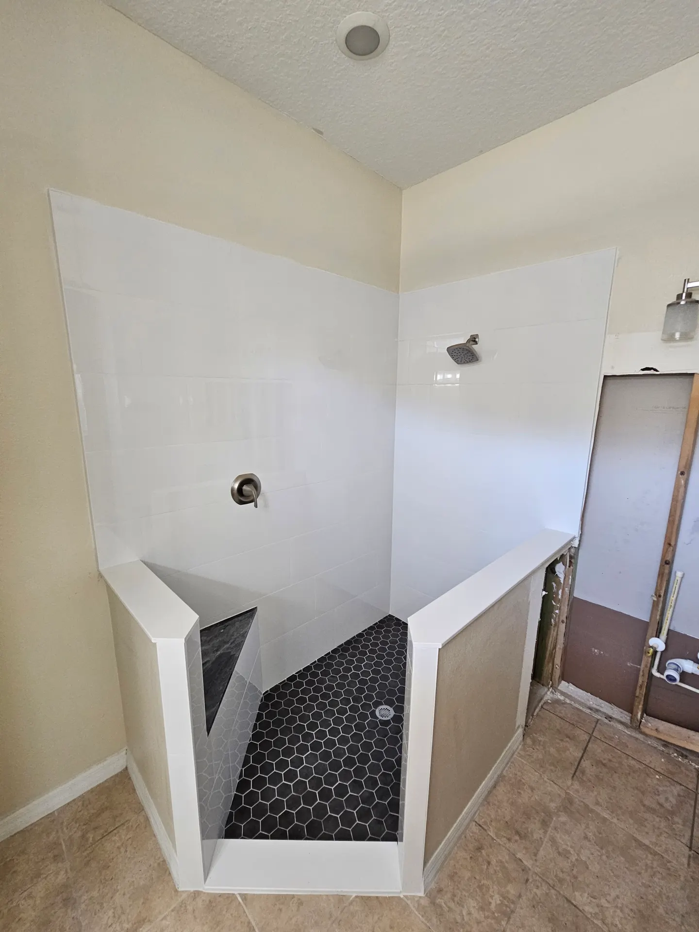 Walk-in shower with glossy white large-format wall tile, a black hexagon mosaic floor, and brushed nickel fixtures mid-renovation.