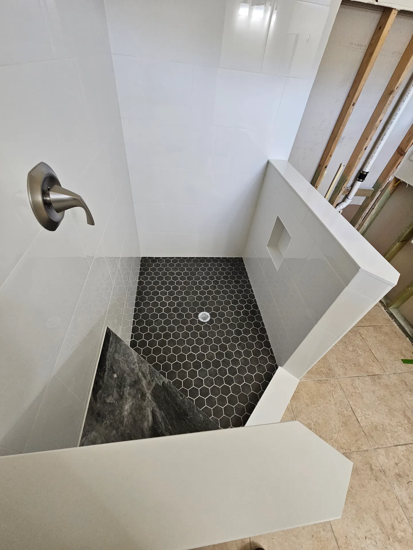 Shower interior detail showing a black hexagon mosaic pan, marble-topped corner bench, recessed niche, and glossy white wall tile.