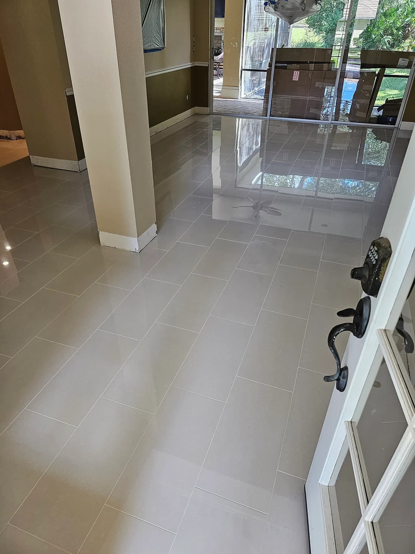 Glossy large-format porcelain tile laid in a staggered brick pattern across an open living and dining area with sliding glass doors.
