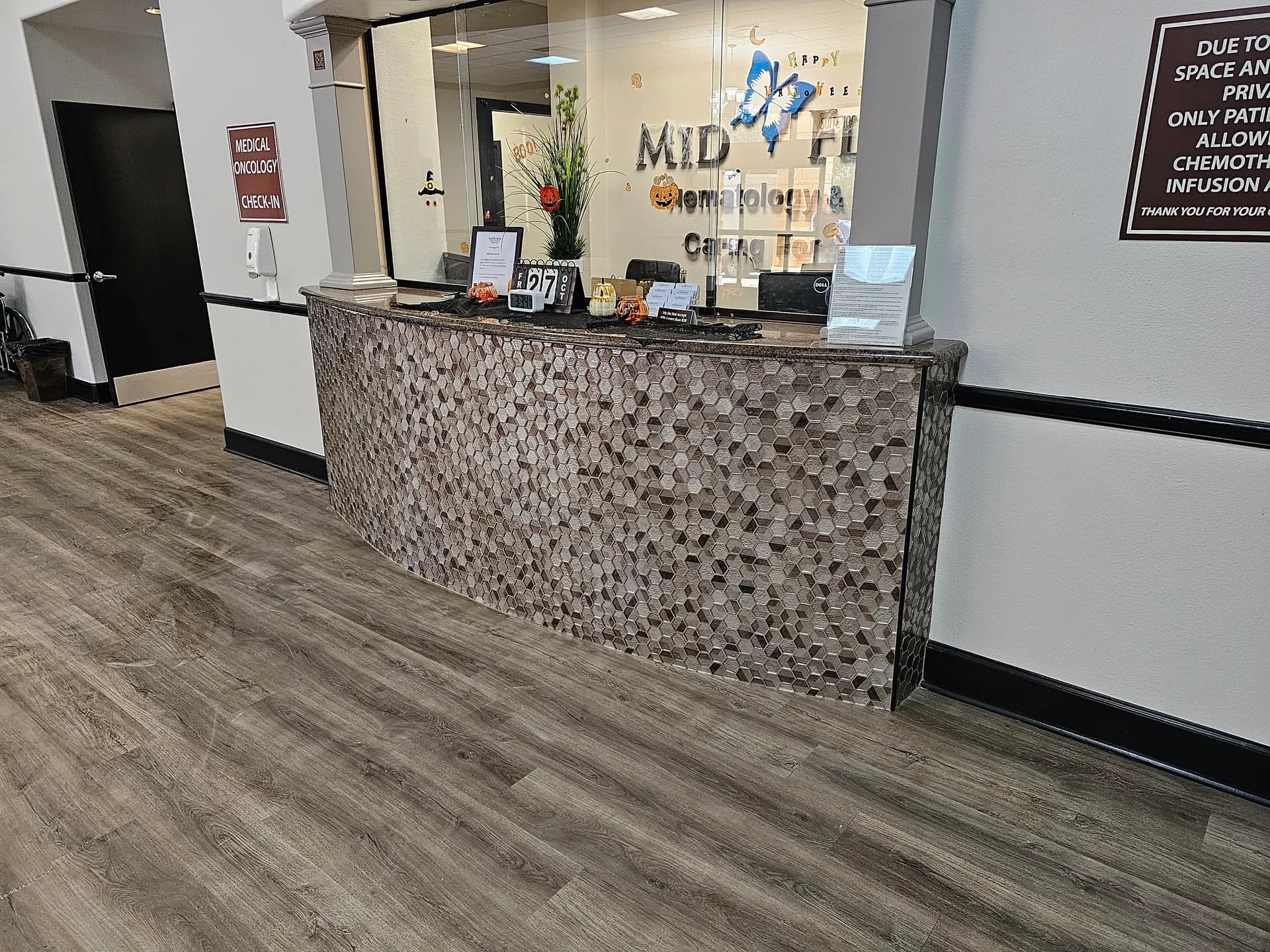 Finished hexagon glass mosaic wrapping a curved granite-topped reception desk in a medical office lobby with wood-look plank flooring.