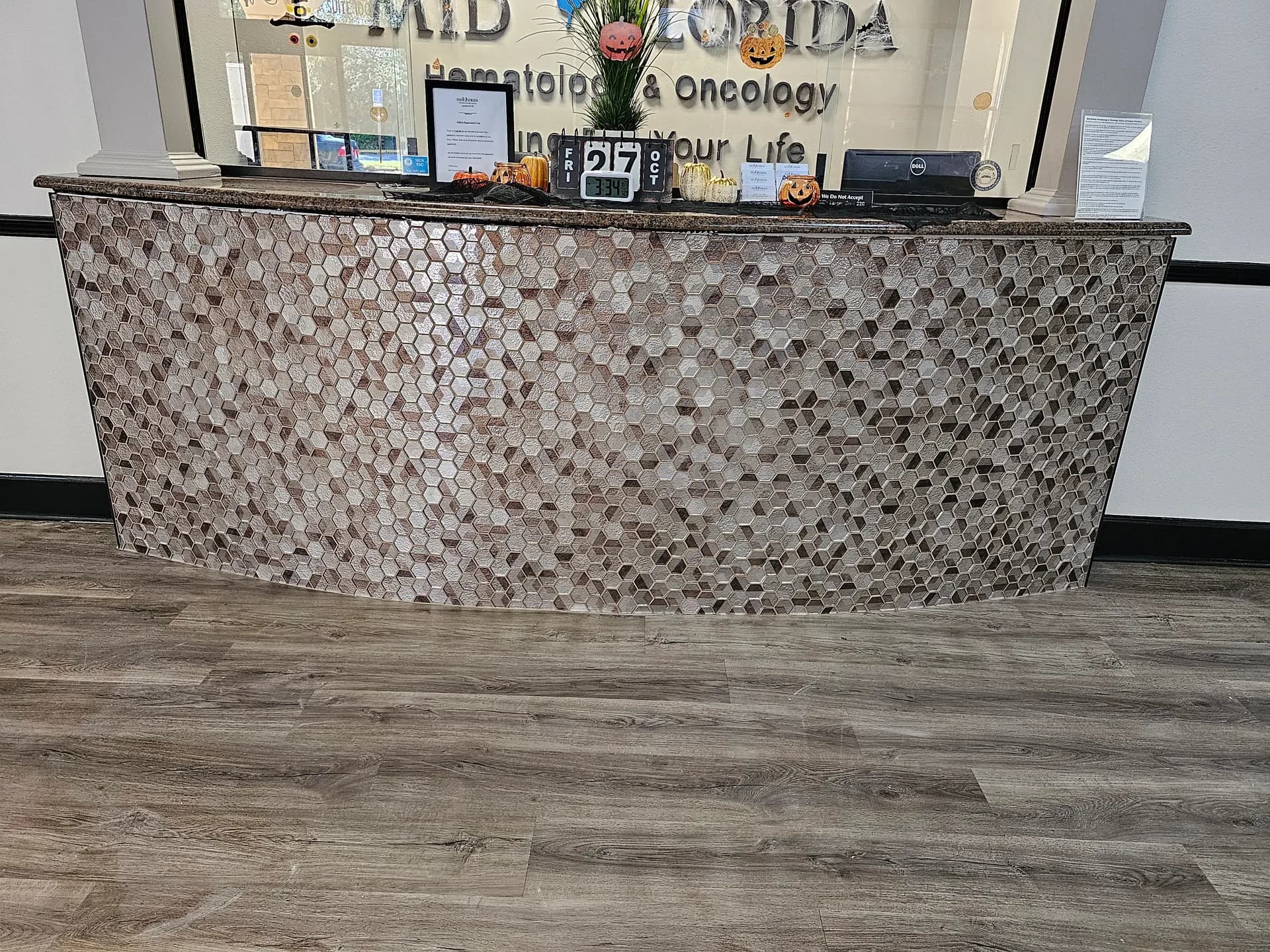 Straight-on view of a shimmering hexagon glass mosaic desk front beneath a granite counter, with wood-look vinyl plank flooring in the foreground.
