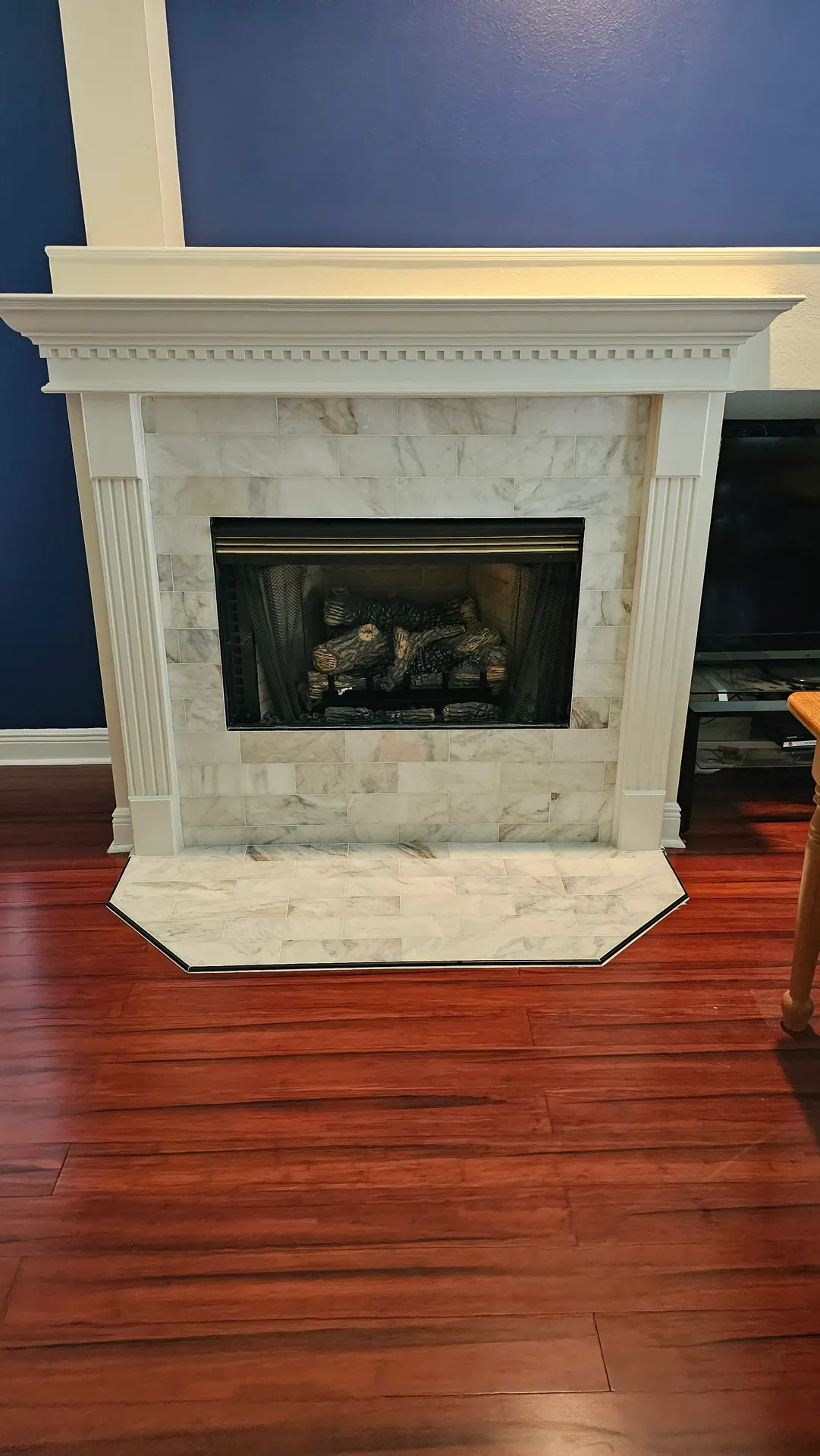 Marble subway tile fireplace surround and matching angled hearth framed by a white classical mantel against a blue accent wall.