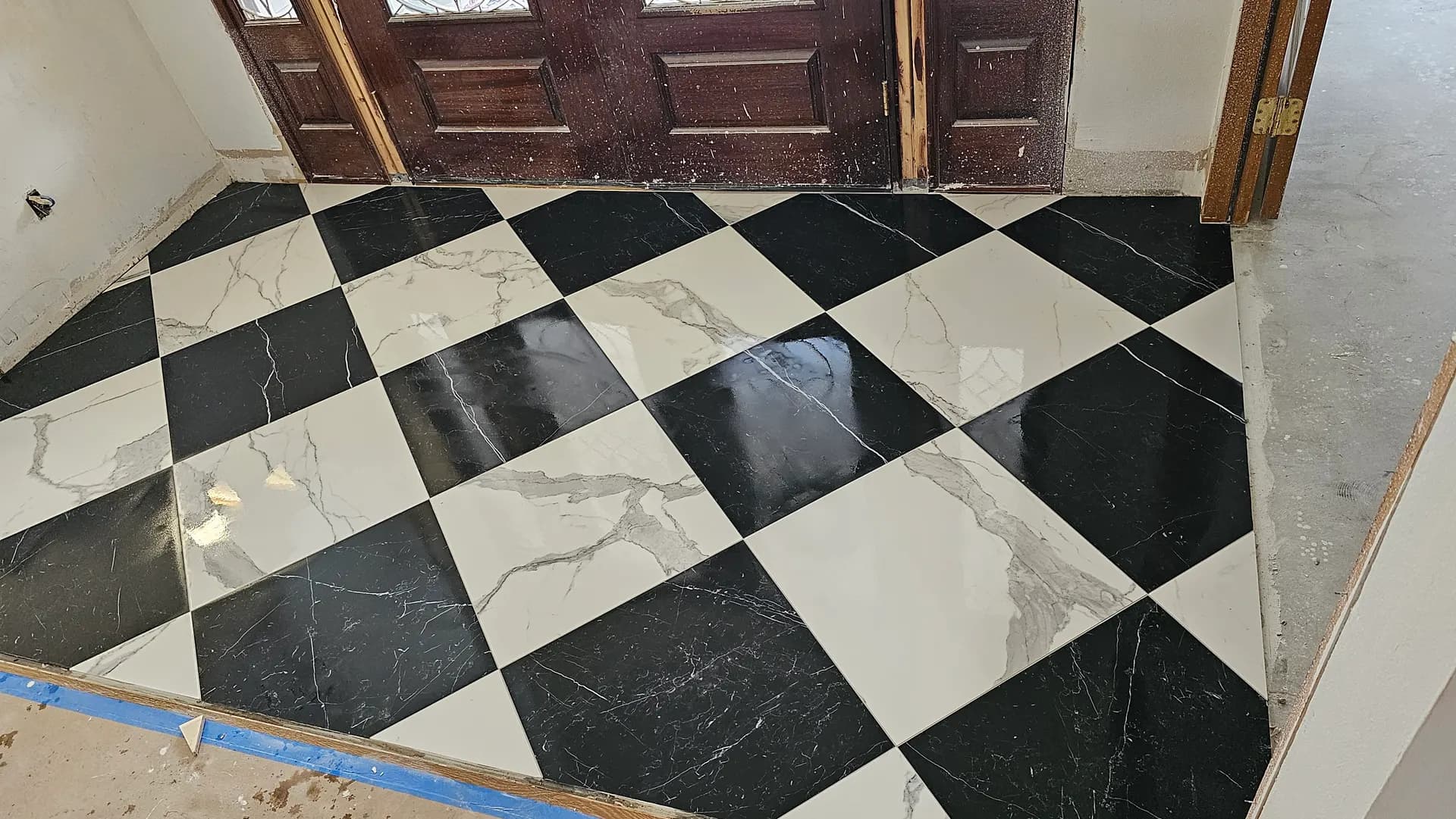 Polished black and white marble-look porcelain tile laid in a diagonal checkerboard pattern in a home entry foyer.
