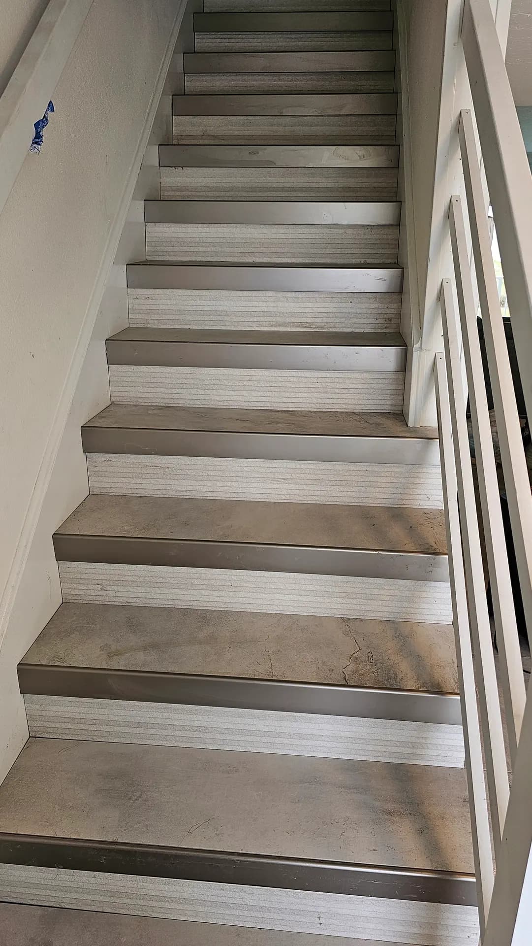 Staircase finished with large-format concrete-look porcelain tile treads and textured tile risers, each step edged with brushed metal stair nosing beneath a white railing.