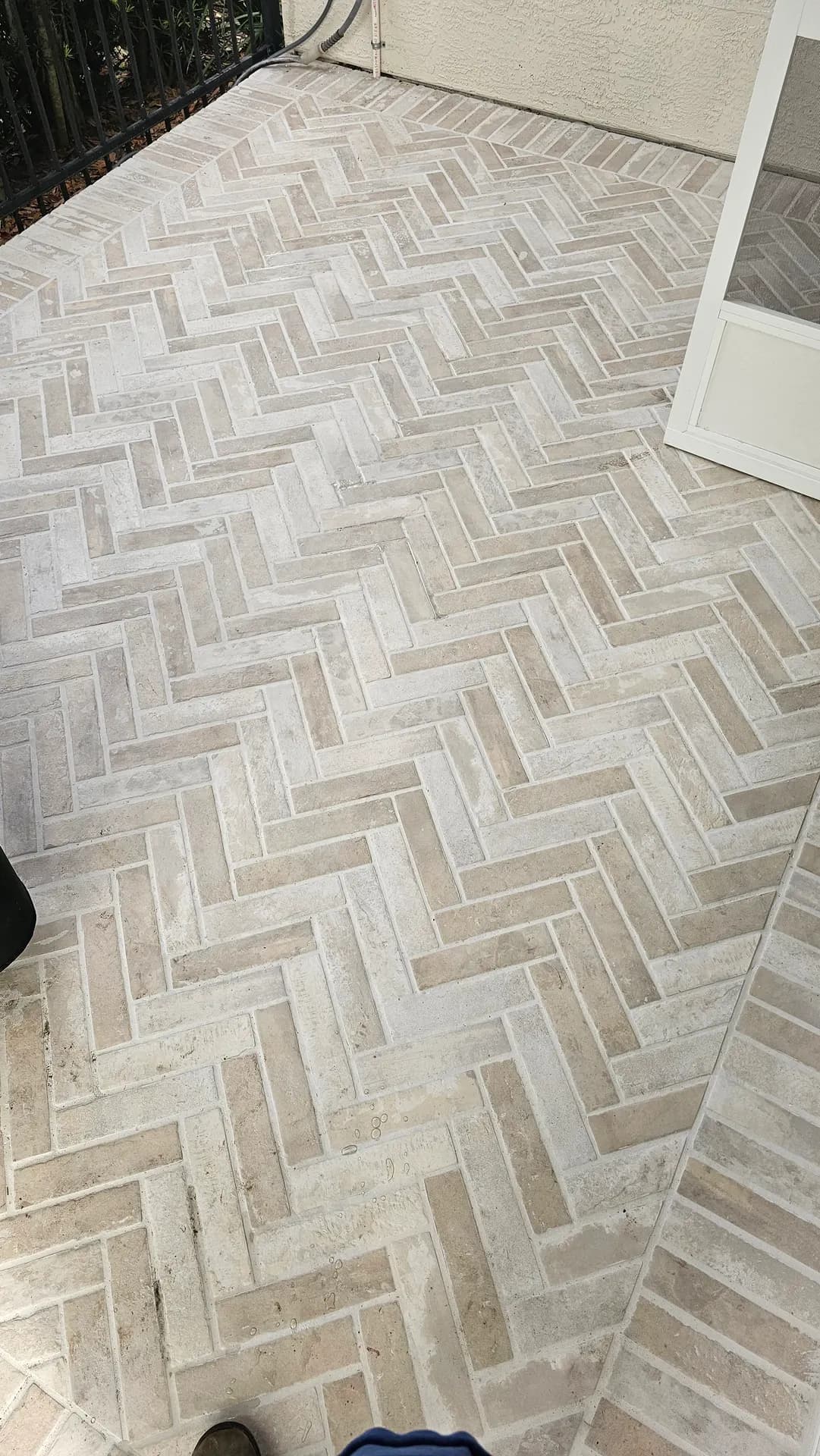 Finished cream and taupe brick-look porcelain tile floor in a herringbone pattern with a straight-lay border on a screened lanai patio.