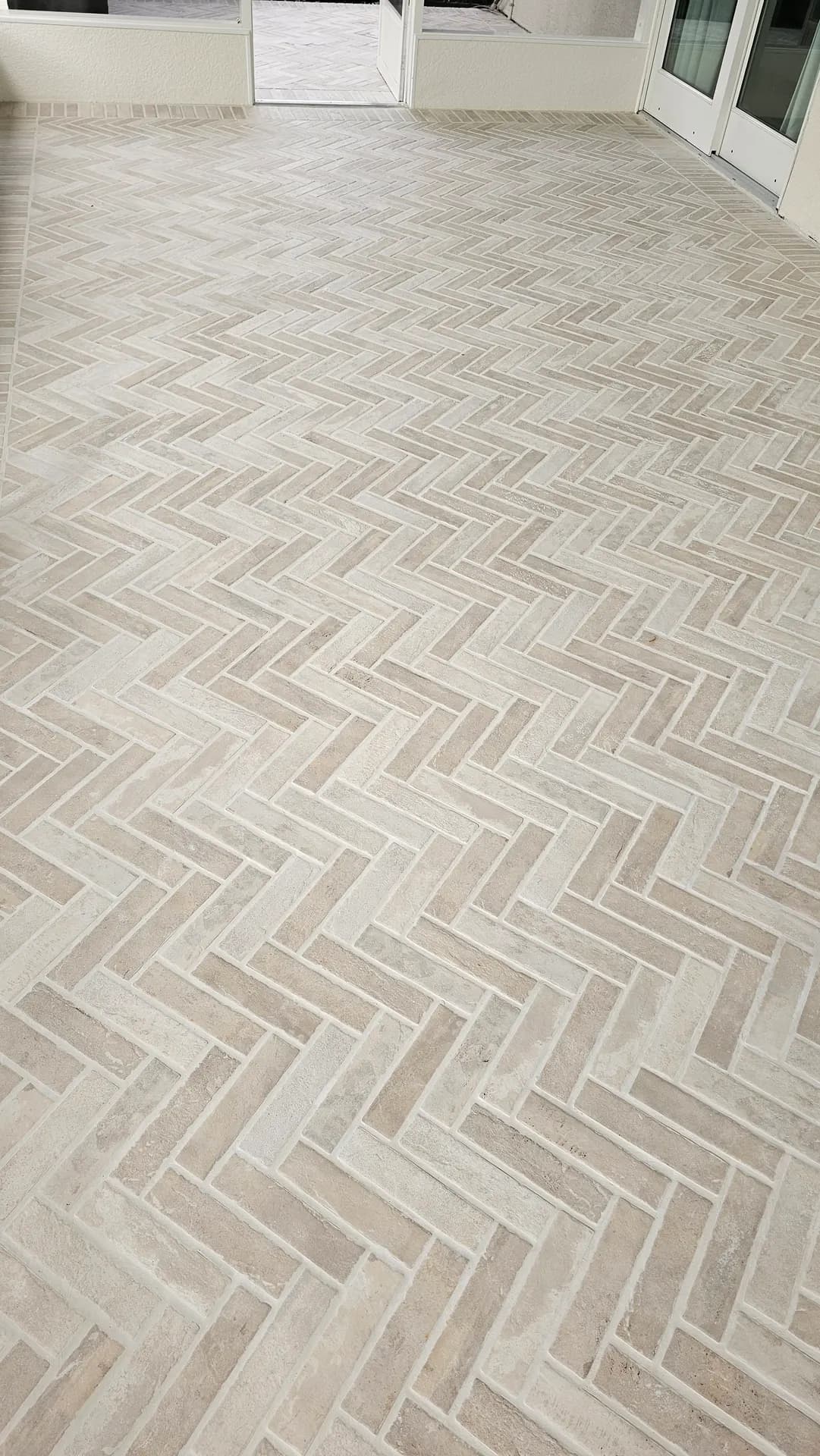 Expansive finished herringbone brick-look porcelain tile floor filling a screened lanai patio in soft natural light.