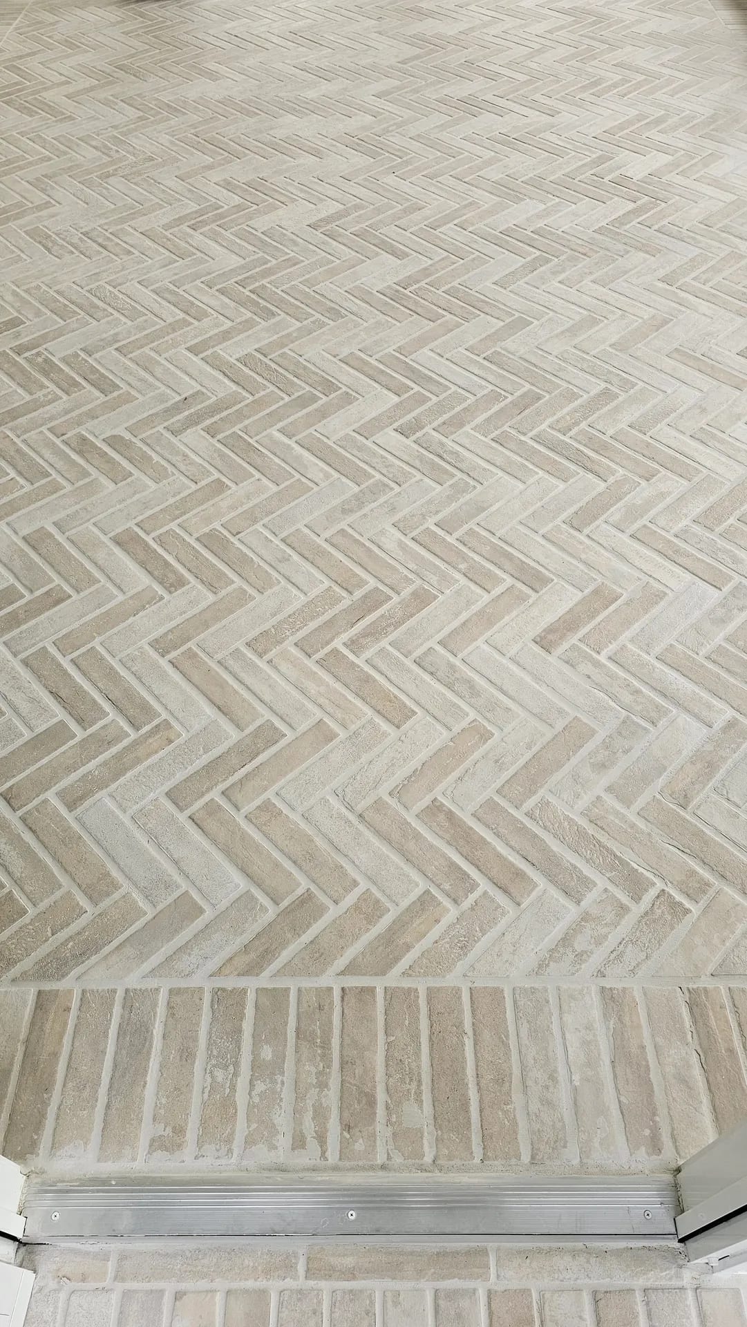 Herringbone brick-look porcelain tile floor meeting a straight-lay border