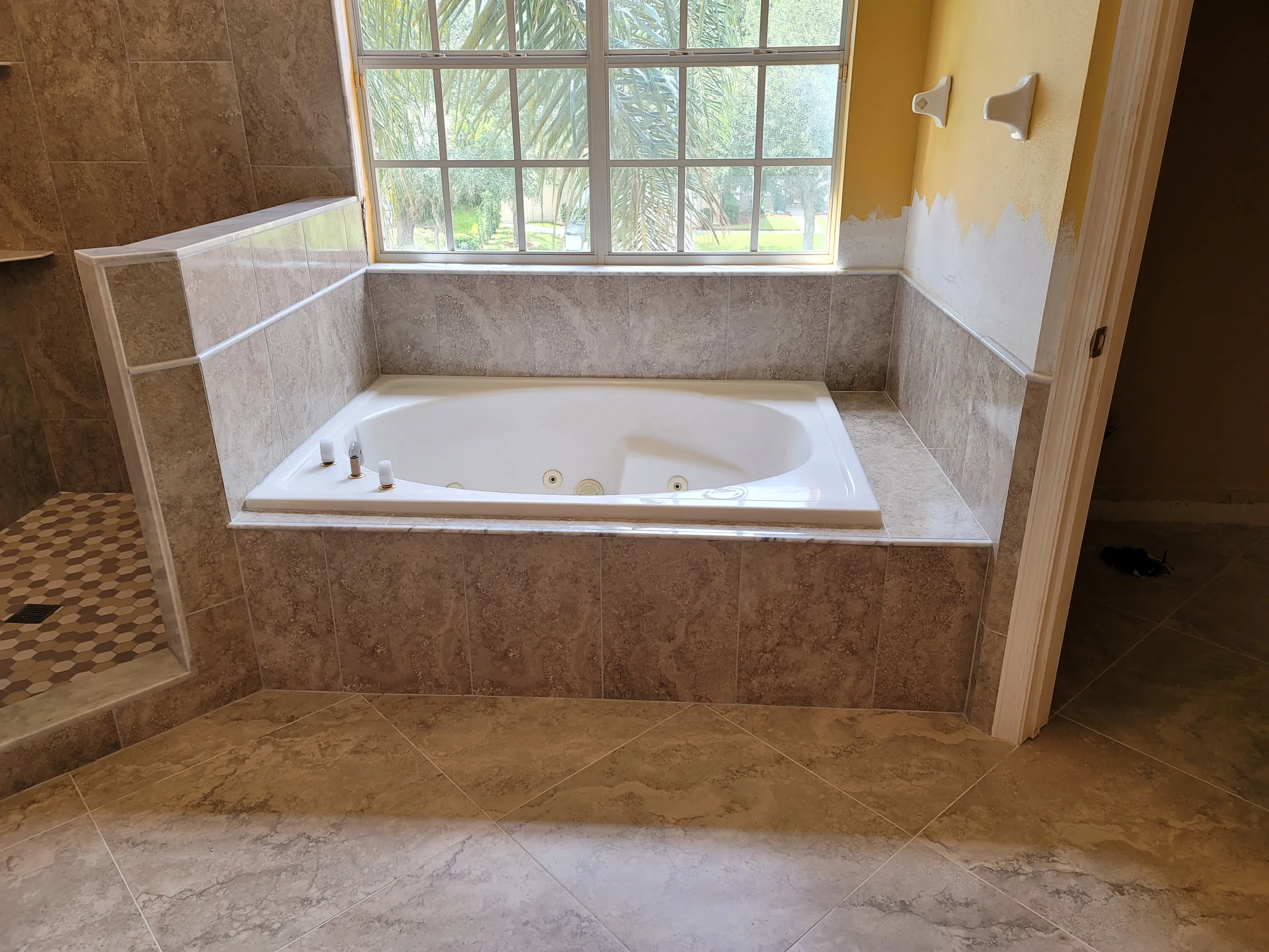Whirlpool garden tub framed by a marble-look porcelain tile surround beneath a large window